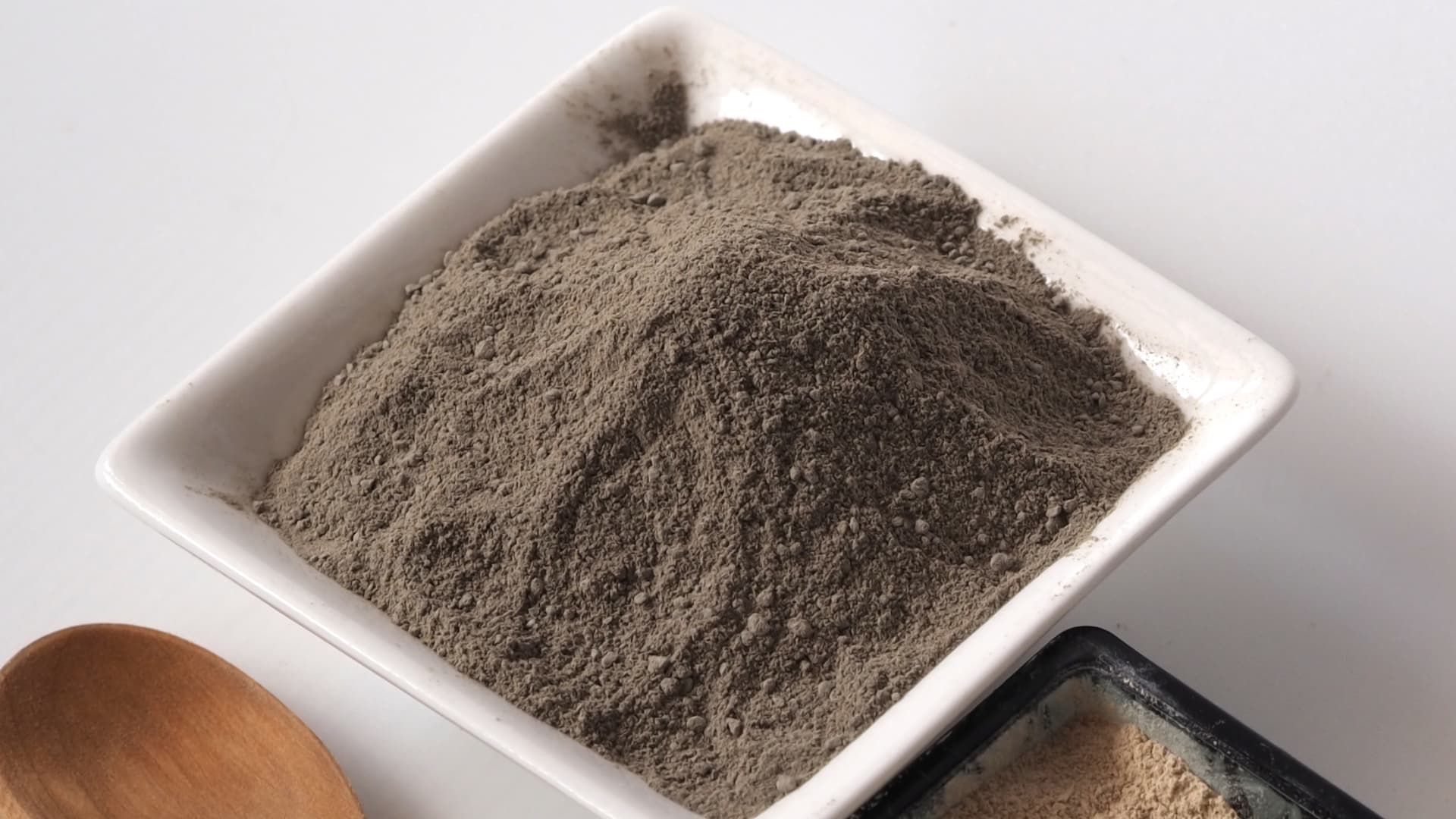 Bentonite Kaolin powder in a white bowl with a wooden spoon on a light gray background