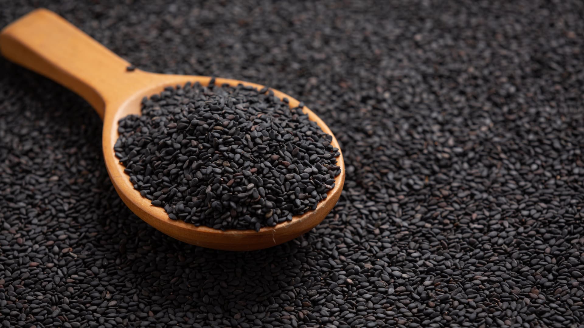 Wooden spoon filled with black cumin seeds on a dark textured background