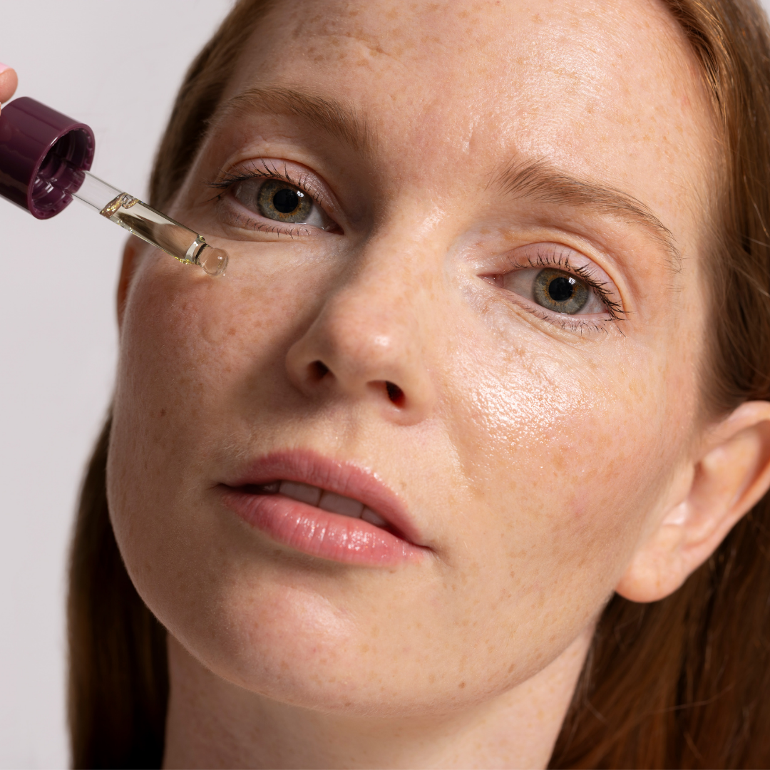 Close-up of a woman's face with a dropper applying Pure Clarity Oil to her skin.