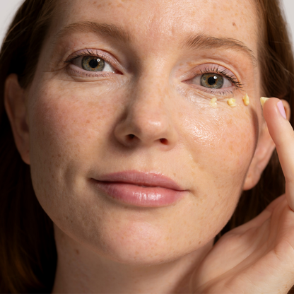 Woman applying Bright Embrace Eye cream to her face with a close-up view.