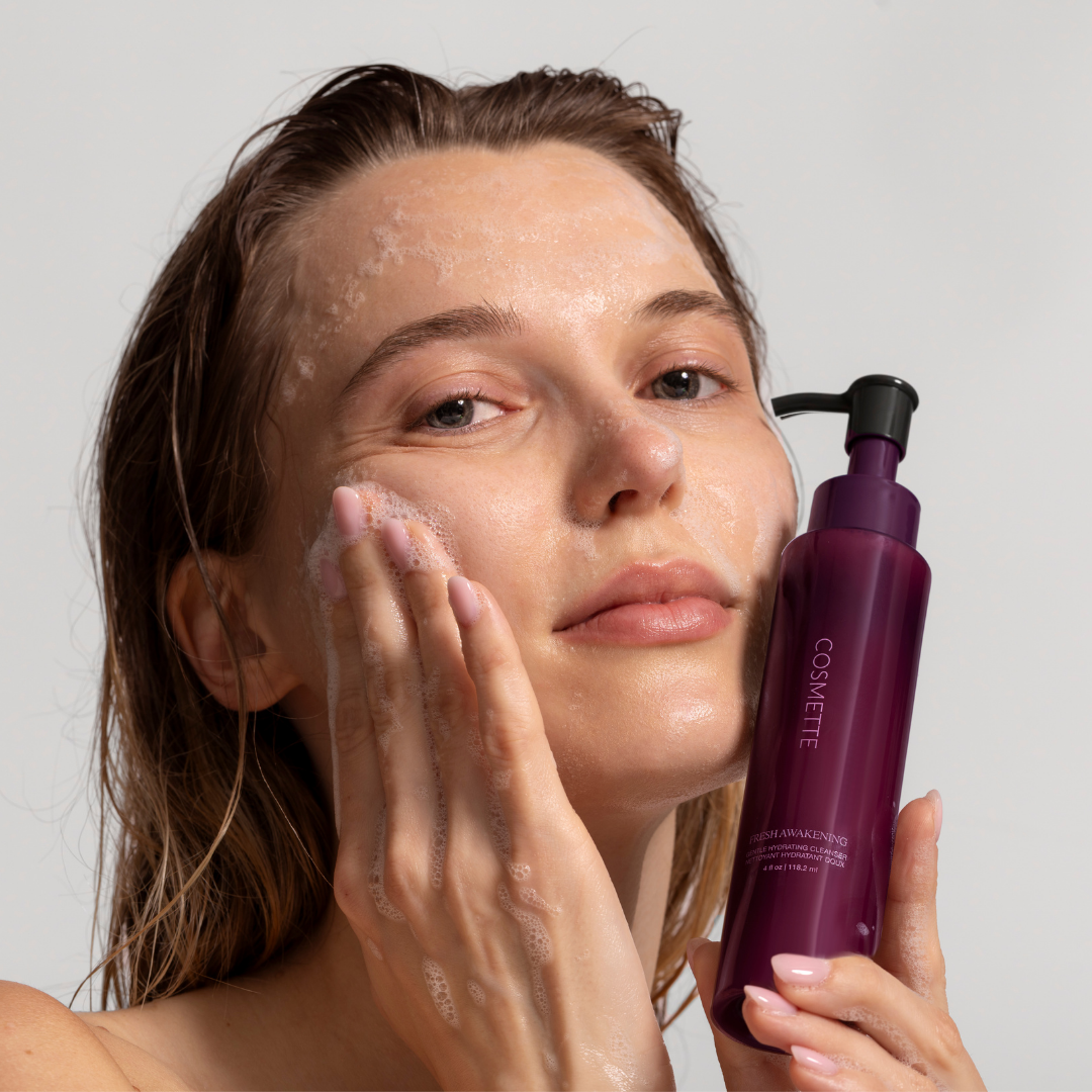 Woman applying Fresh Awakening Cleanser with Cosmette bottle on a plain background