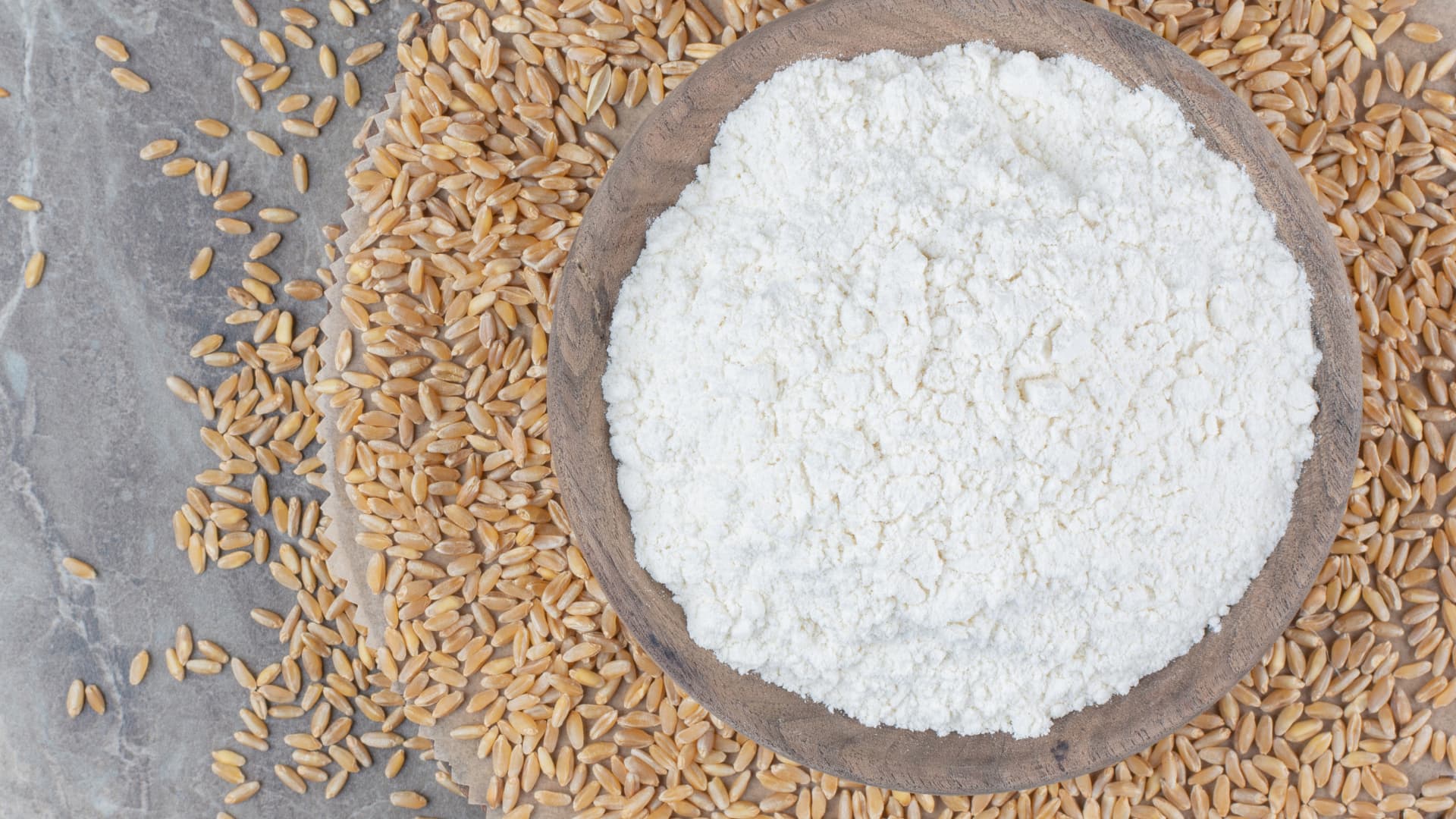 White rice in a wooden bowl surrounded by uncooked rice grains on a stone surface