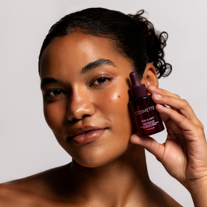 Woman holding a cosmette Pure Clarity Oil dropper bottle near her face against a neutral background